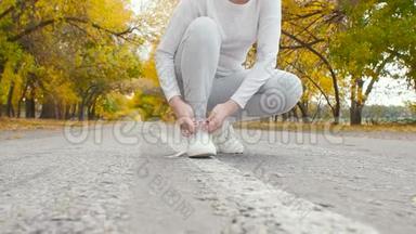在秋天的大自然中，在沥青跑道上系鞋带的跑步者，年轻的女人准备开始跑步，女孩从事户外运动，